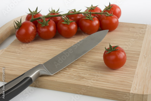 Bunch of cherry tomatoes with green leaves lying on a cutting board  isolated on white background. Still-life studio shot taken with soft-box.