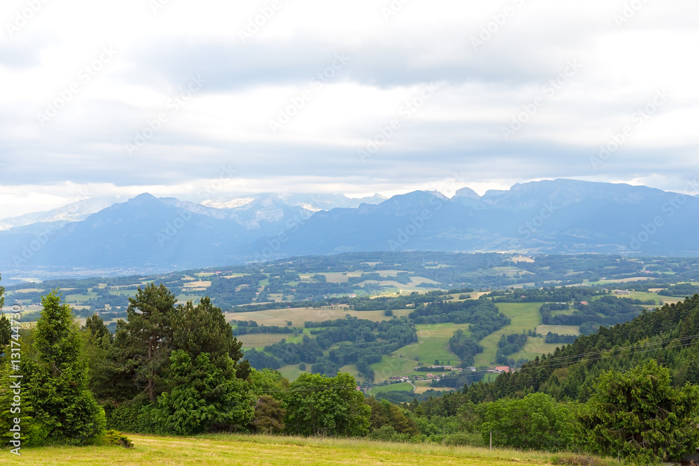 Obraz premium Panoramic view of Swiss Alps near Geneva, Switzerland. Farmhouses and hilly countryside on a cloudy day in summer.