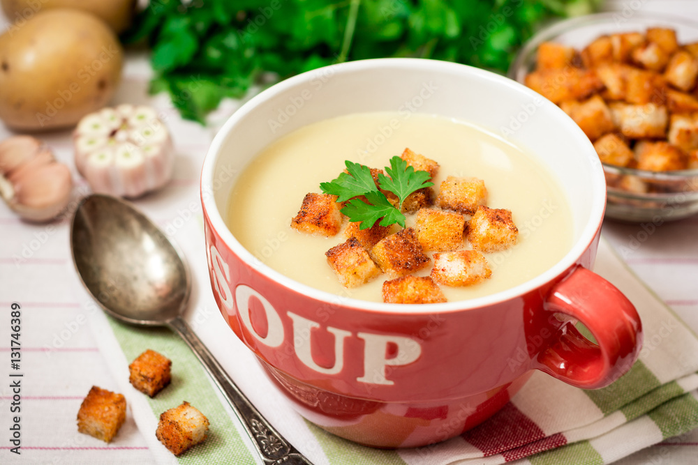 Homemade potato cream soup with croutons and parsley in red bowl on table Homemade potato cream soup with croutons and parsley in red bowl on table