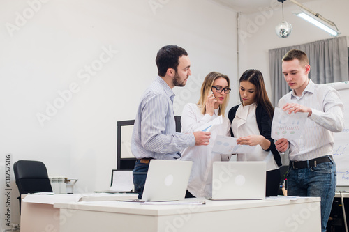 Group of four diverse men and women in casual clothing talking in office