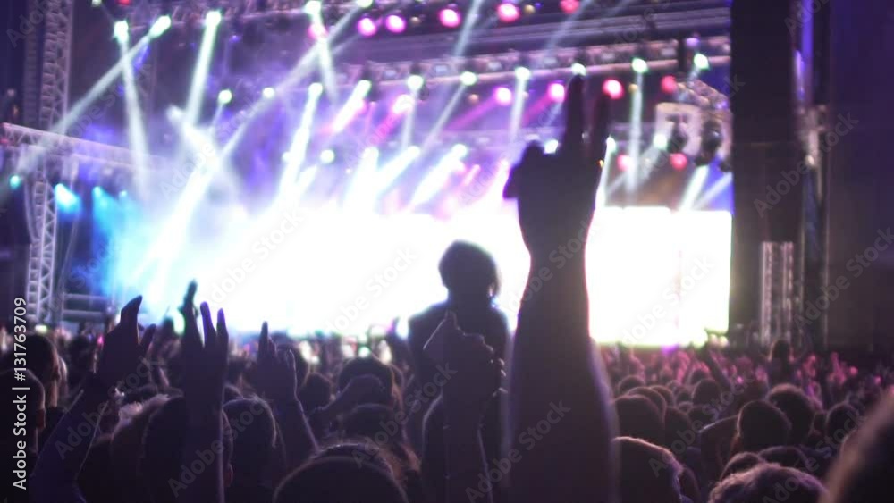 Shadows of excited audience jumping at concert with hands raised in air, slow-mo