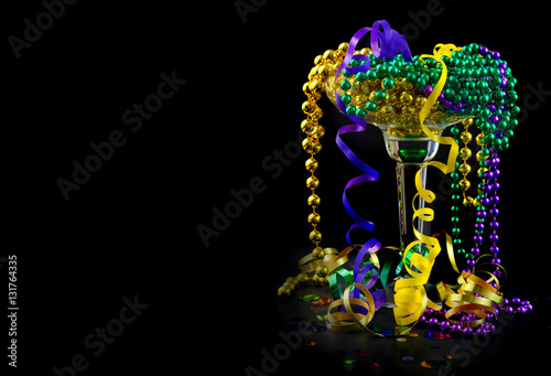 Fototapet Mardi Gras image of purple, green and gold beads and ribbons spilling out of a party drink glass on black background