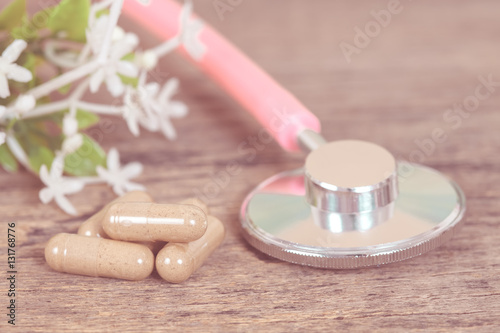 herb capsules and stethoscope on wood table