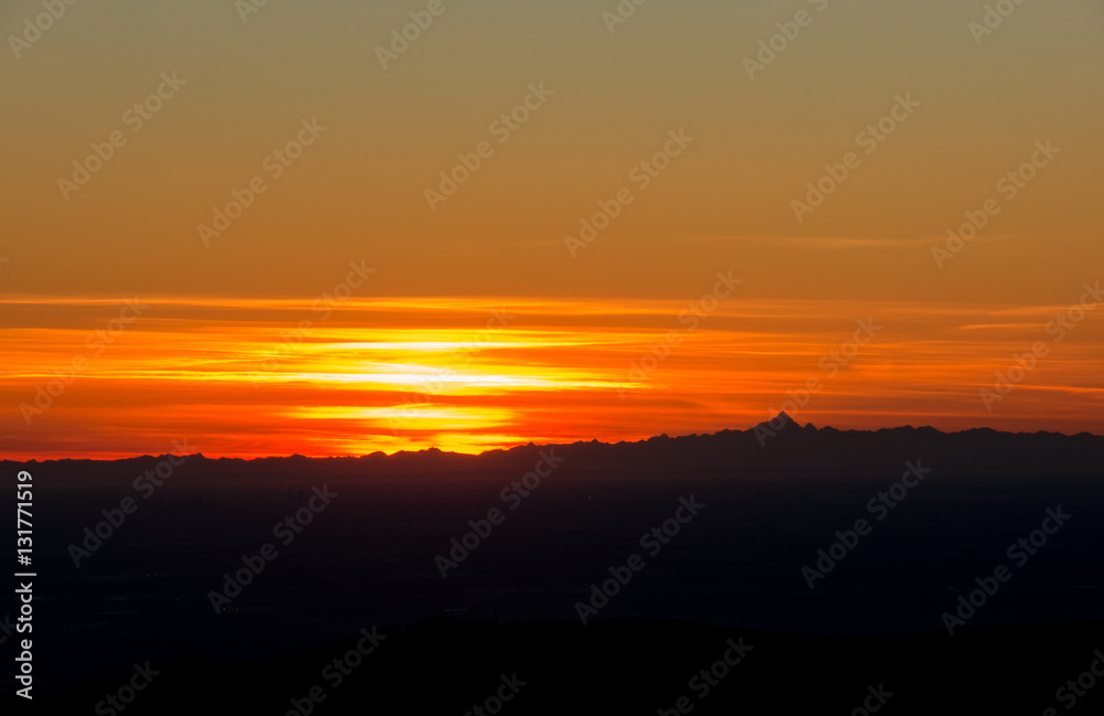 Fiery sunset from mountain pick with thin glazes in the sky evening. Fall season. Orobie alps. Rena pick. Bergamo Italy. In the distance the Monviso.