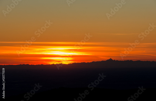 Fiery sunset from mountain pick with thin glazes in the sky evening. Fall season. Orobie alps. Rena pick. Bergamo Italy. In the distance the Monviso.