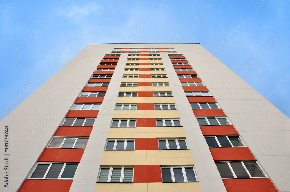 White facade of a modern multistory highrise residential building with red, yellow inserts. Look up, symmetry view. White facade of a modern multistory highrise residential building with red, yellow inserts. Look up, symmetry view.
