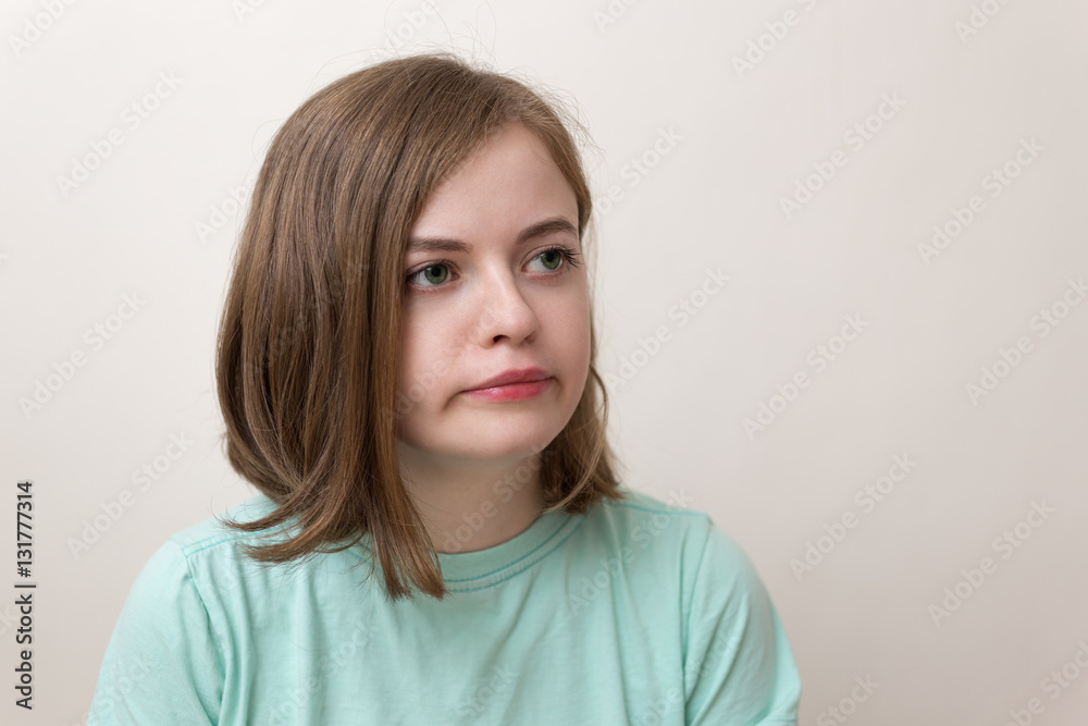 Semi-profile of a blond girl in a blue t-shirt with an annoyed, funny, bored or tired expression on her face with white background and soft colors Semi-profile of a blond girl in a blue t-shirt with an annoyed, funny, bored or tired expression on her face with white background and soft colors