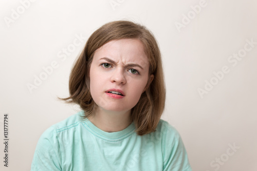 Indoor portrait of beautiful girl with bob hairstyle in blue green t-shirt with questioning expression on her face as if asking What? in disbelief or suspicions. White background