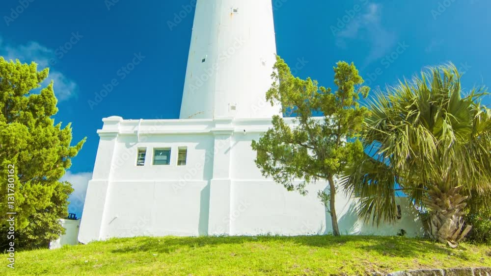 Tilting-up to Gibb's Hill Lighthouse Tower in Southampton, Bermuda on a Sunny Day with Green Grass and Trees, a Stone Wall and a Blue Sky Background