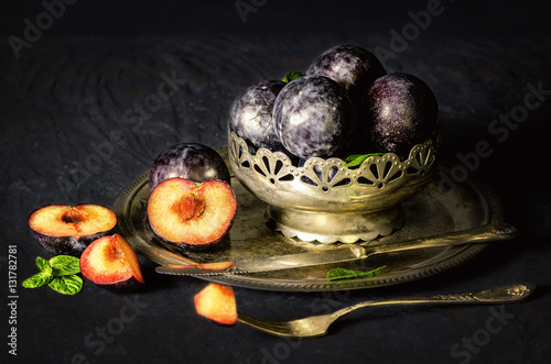 Classic still life with fresh plums placed in silver vintage plate on dark background..
