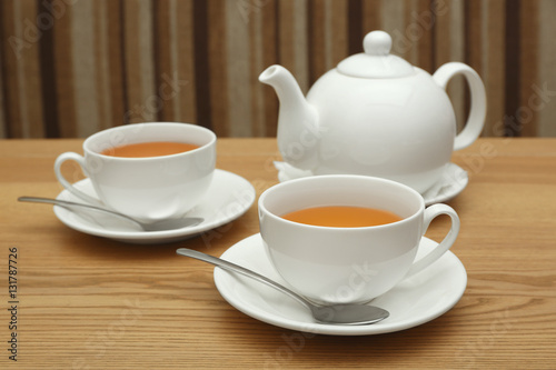 Two cups of hot tea and teapot on wooden table