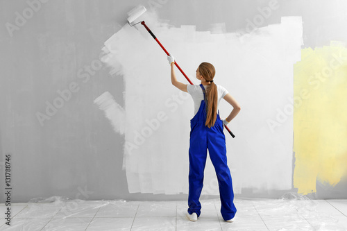 Beautiful young woman painting wall in room