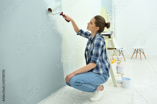 Beautiful young woman painting wall in room photo