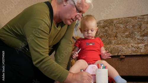 Attractive baby sitting on the pot and drawing with her grandfather markers on paper. The boy peeing and playing with the family home. Kid 1 year.