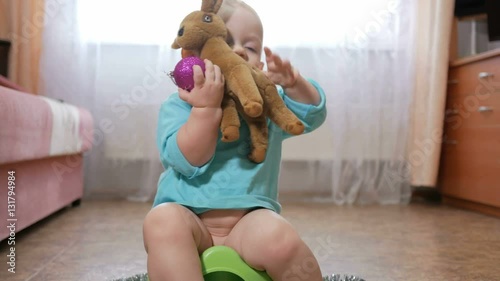 Attractive baby sitting on the pot and playing with teddy deer. In the hands of the New Year's ball and decoration for the Christmas tree. The concept of the family new year