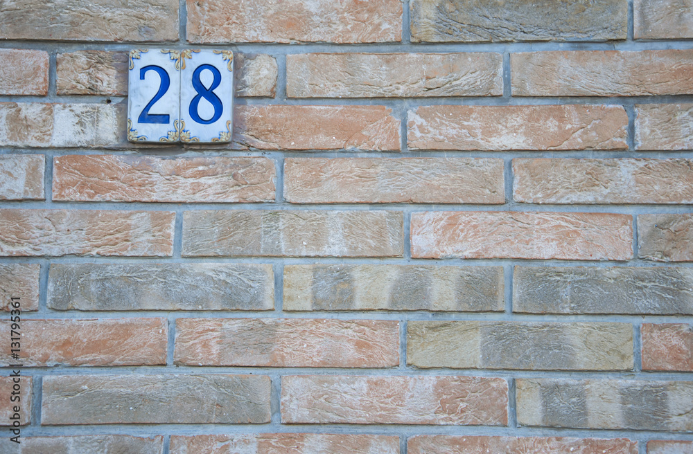 Traditional Italian home sign board painted on ceramic tile placed on orange wall, with number 28. Traditional Italian home sign board painted on ceramic tile placed on orange wall, with number 28.