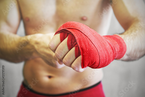 Man is wrapping hands with red boxing wraps.