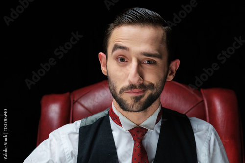 close portrait of handsome male model in black suit fixing his red tie while looking at the camera in smile