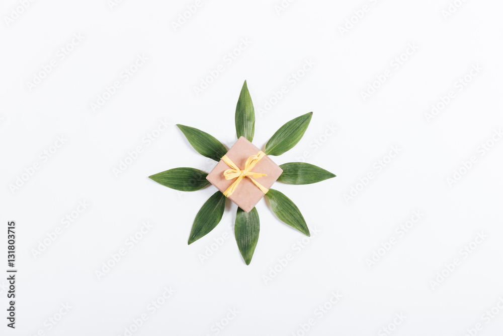 Small box with a gift and yellow bow with petals on a white tabl Small box with a gift and yellow bow with petals on a white tabl
