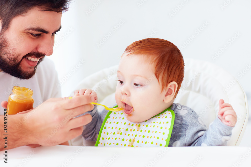 happy father feeding cute redhead baby with complementary food happy father feeding cute redhead baby with complementary food