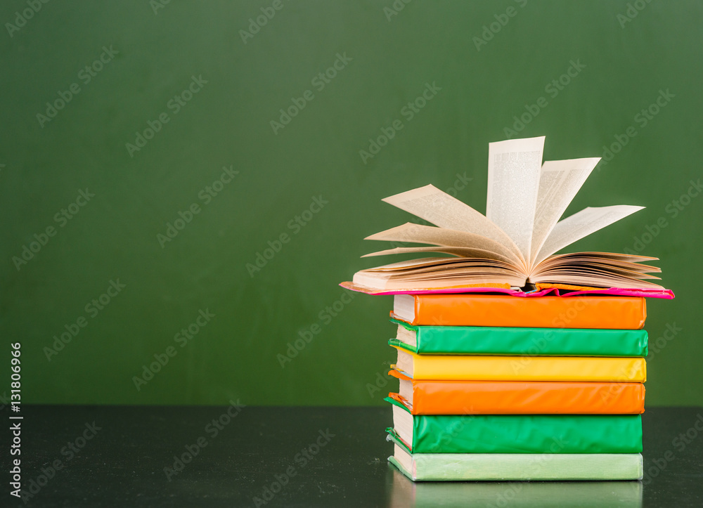 Open book on stack of books near empty green chalkboard. space for text Open book on stack of books near empty green chalkboard. space for text