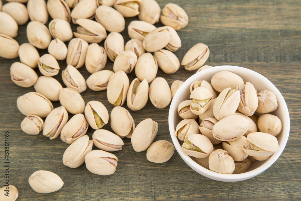 White bowl of pistachios on wooden background