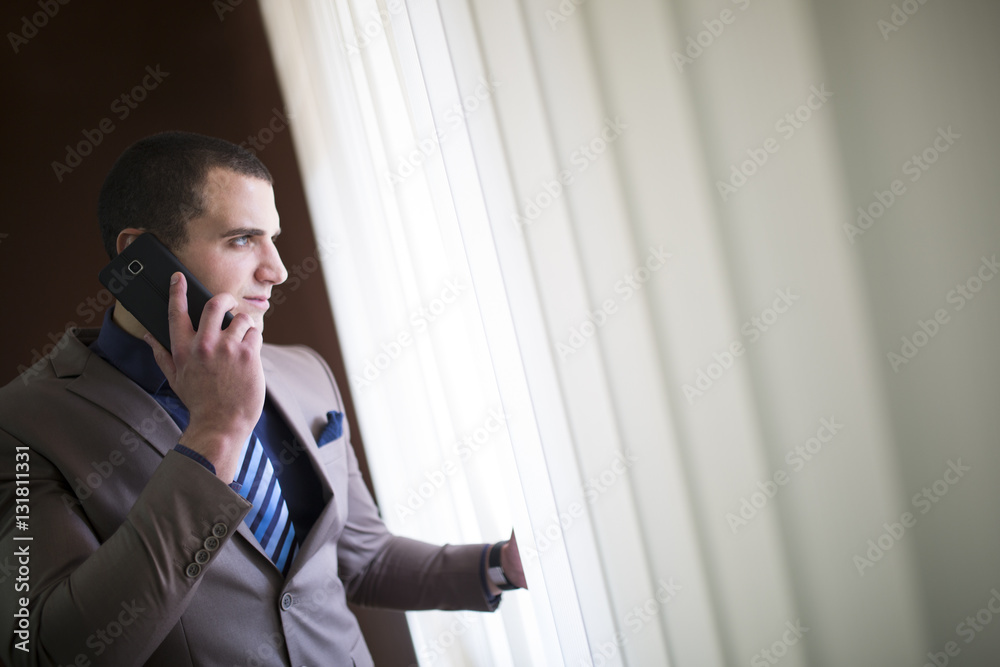 Young handsome businessman talking on the phone while looking through the window. Young handsome businessman talking on the phone while looking through the window.