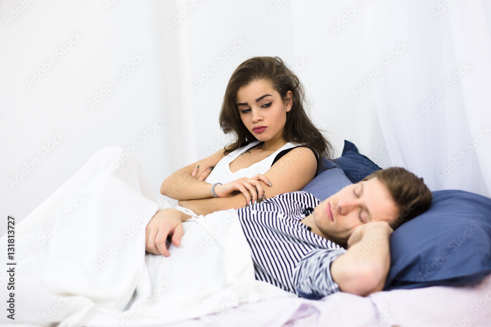 Man sleeping in bed and snoring loudly while his wife sitting near by him and looking at him. Pretty tired lady dreaming about sleeping all time. Man sleeping in bed and snoring loudly while his wife sitting near by him and looking at him. Pretty tired lady dreaming about sleeping all time.