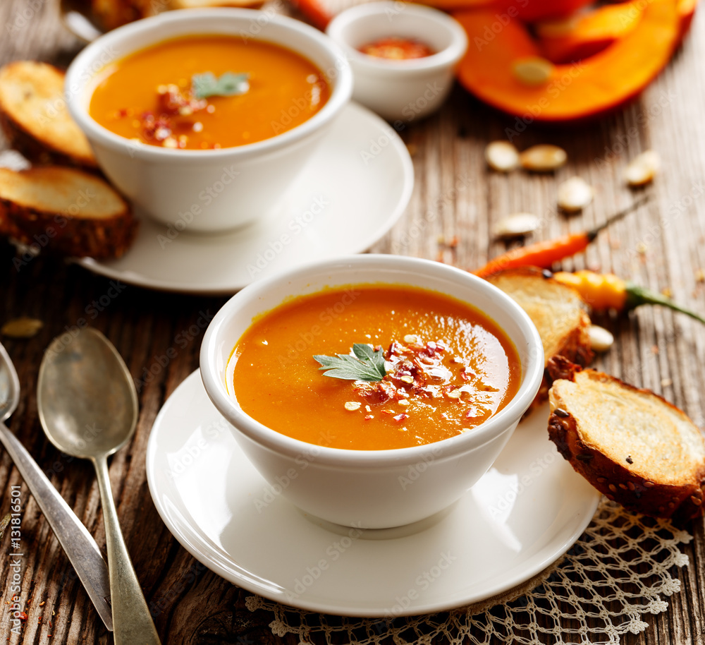 Homemade pumpkin soup in a white ceramic bowl on a wooden rustic table, nutritious and delicious vegetarian dish Homemade pumpkin soup in a white ceramic bowl on a wooden rustic table, nutritious and delicious vegetarian dish
