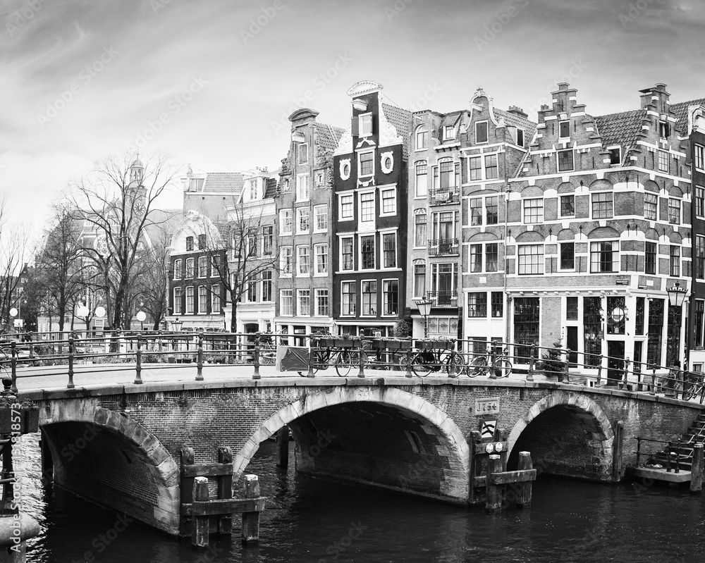 Naklejka premium Kanał Prinsengracht, Amsterdam, Holandia. Typowe holenderskie domy ze szczytem schodkowym za mostem. Czarny i biały.
