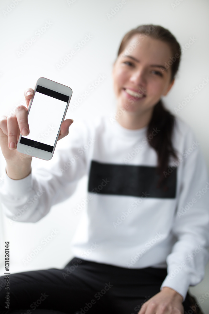 Young woman showing screen on her smartphone against white background Young woman showing screen on her smartphone against white background