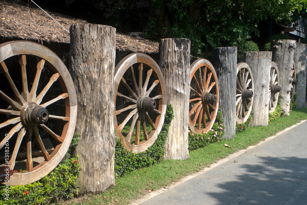 An old wheel of a traditional cart leaning on a wooden fence.