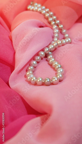 Beads from pearls against the background of pink fabric.