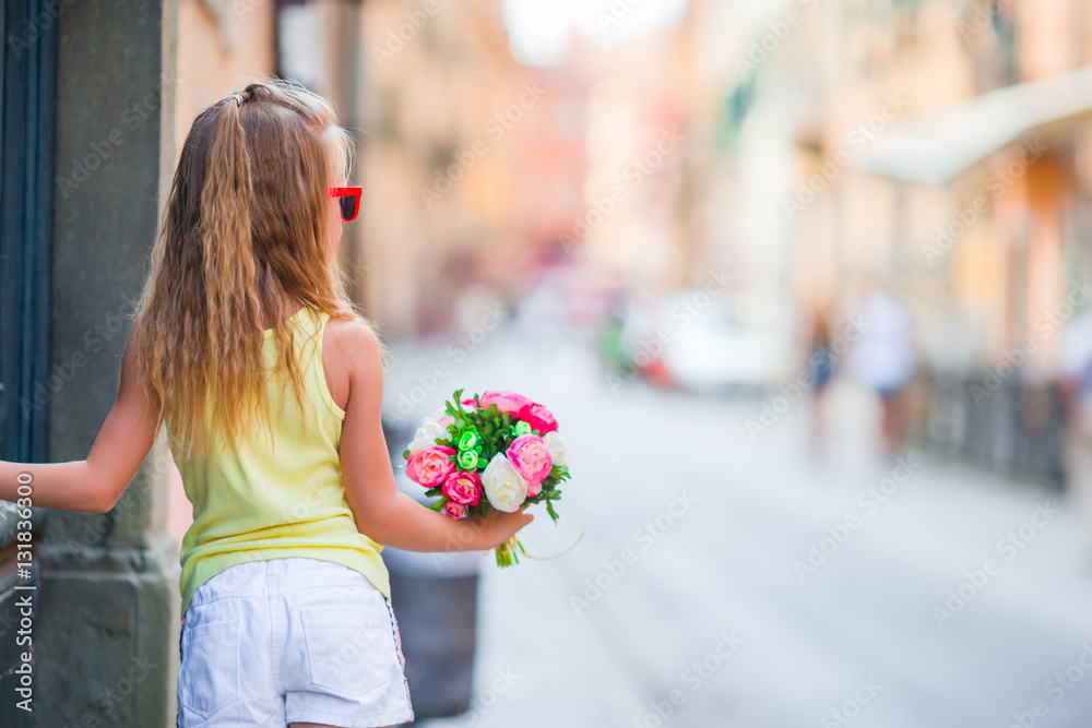 Fototapeta premium Adorable little girl with flowers bouquet walking in european city