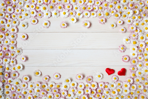 Wooden light background with daisies and red hearts