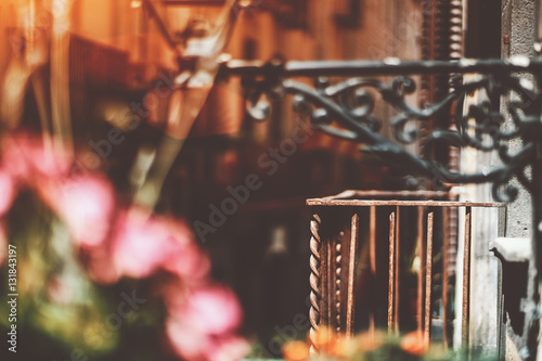 Empty old rusty metal balcony with blurred narrow street behind and lantern with pink flowers in front, historical district of Barcelona - El Born on sunny summer day, Spain