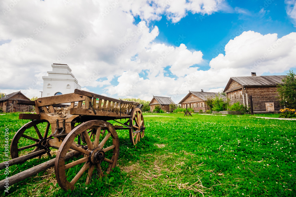Obraz premium Country landscape with huts and wooden wagon in the foreground