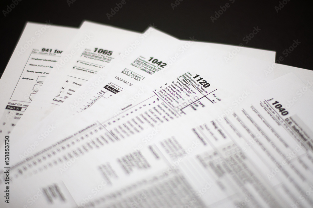 Tax Season: Horizontal left side view of 1040 U.S. Individual Income Tax Return Form with an office laptop background with red white pen and eye glasses foreground Tax Season: Horizontal left side view of 1040 U.S. Individual Income Tax Return Form with an office laptop background with red white pen and eye glasses foreground