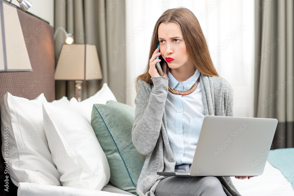 Displeased business woman calling with phone in the luxury hotel room. Staying at the hotel during the business trip Displeased business woman calling with phone in the luxury hotel room. Staying at the hotel during the business trip