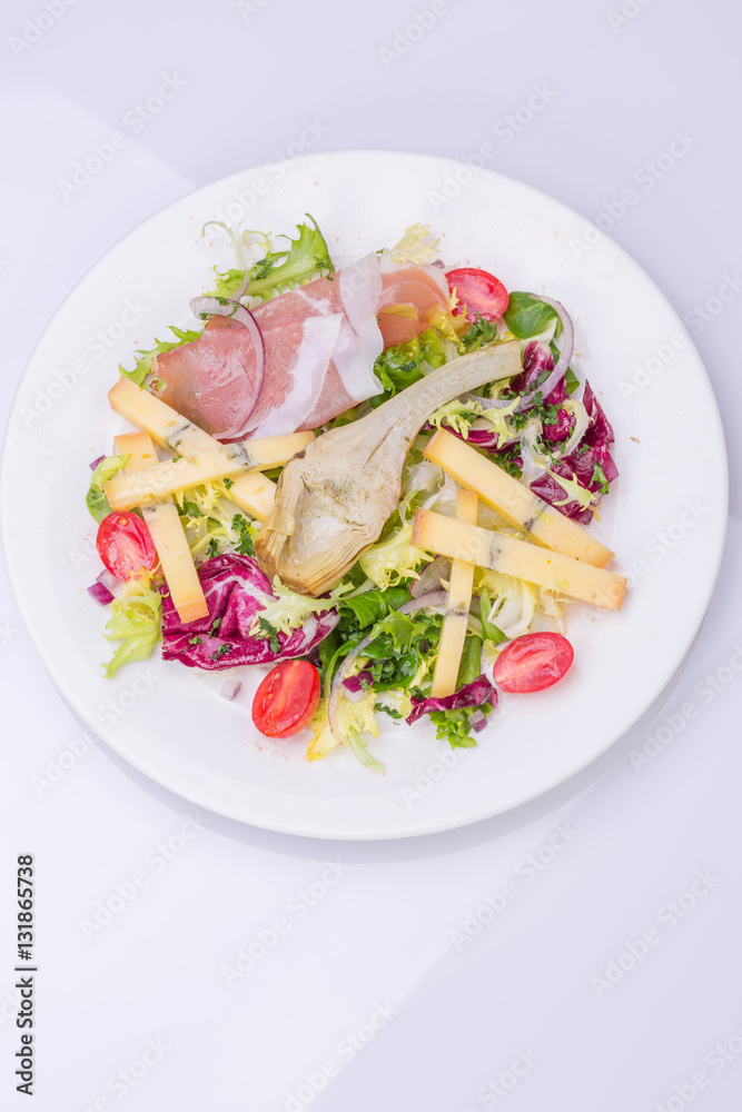 mix salad with fresh vegetables and cheese on a white plate. cherry tomato salad, lettuce, marinated artichoke, onion, cheese, ham