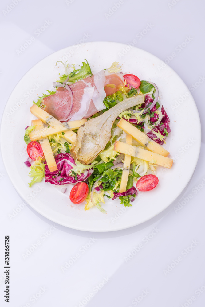 mix salad with fresh vegetables and cheese on a white plate. cherry tomato salad, lettuce, marinated artichoke, onion, cheese, ham mix salad with fresh vegetables and cheese on a white plate. cherry tomato salad, lettuce, marinated artichoke, onion, cheese, ham