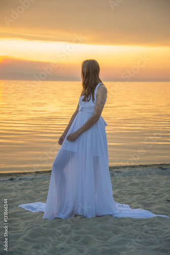 Beautiful girl in a long white dress walking on the seaside.