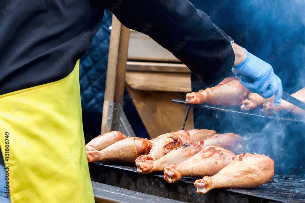 Close-up of a hands  man, dressed in  black shirt and in  yellow apron, cooking turkey legs on the hot grill