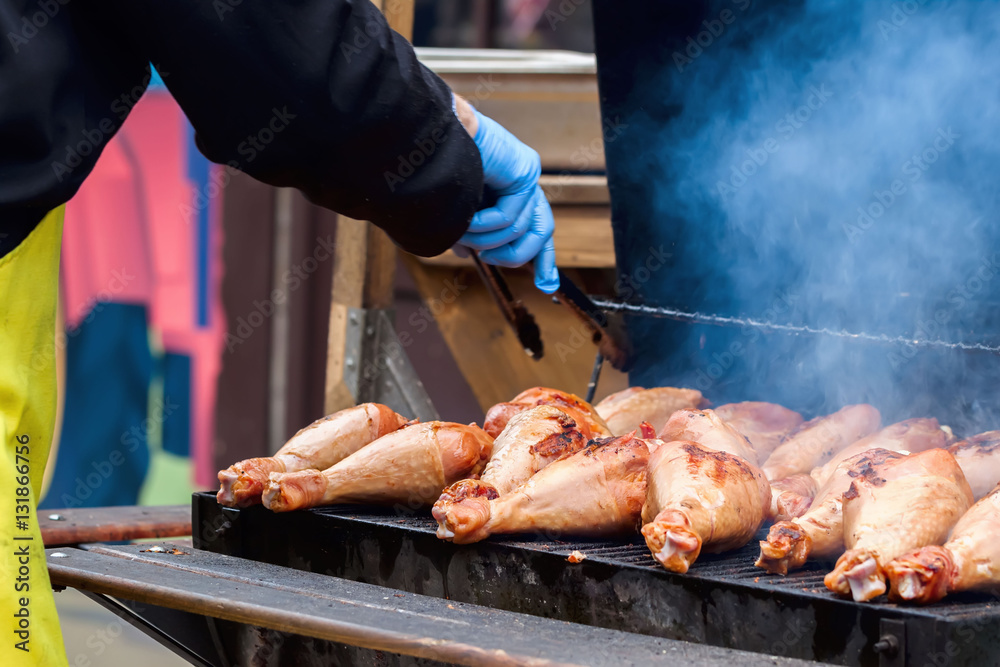 Man's hand with a Grill tongs flips turkey legs fillets on the barbecue to not burnt.