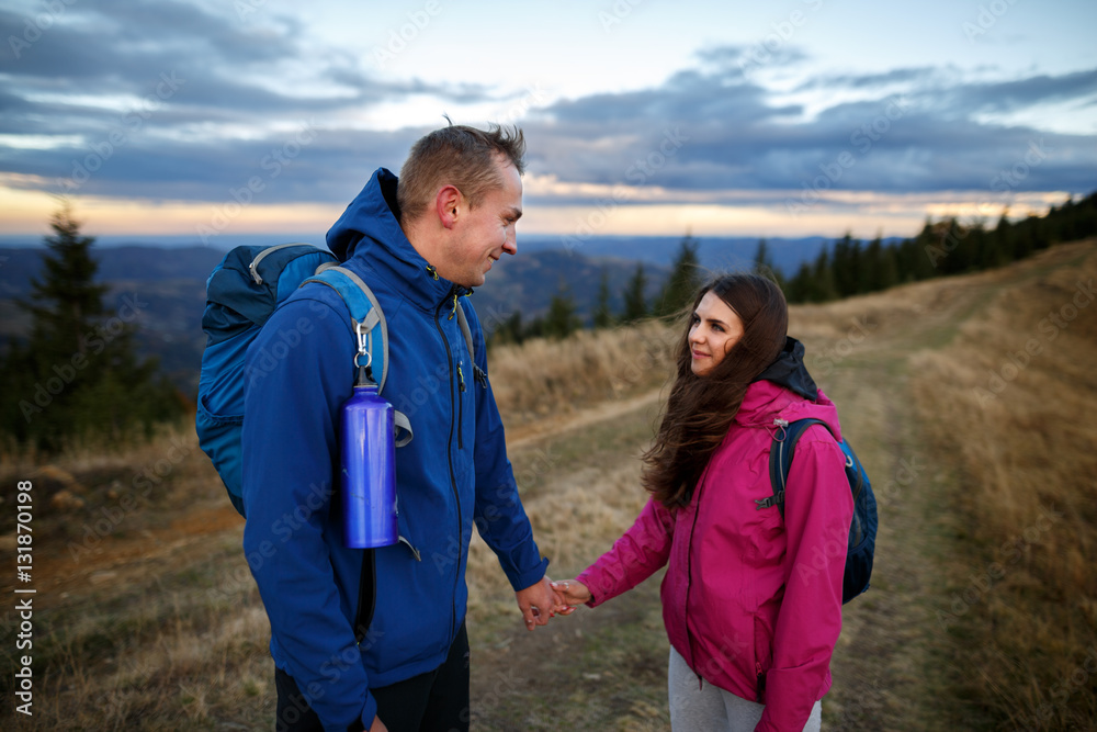 Young couple hiking outdoors with backpacks during sunset