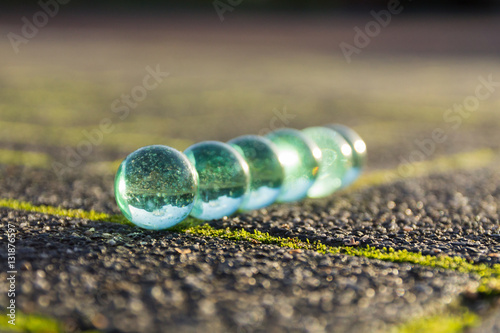 Translucent glass marbles on the sidewalk.
Neatly arranged in the light of the setting sun.