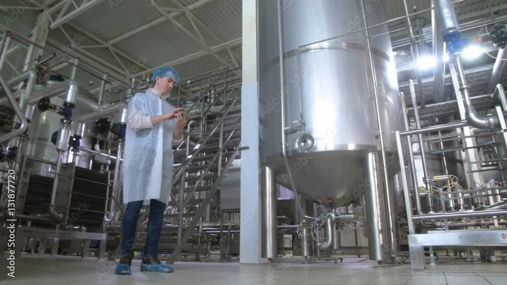 Worker in brewery near tanks, pipeline working with tablet. 4K. Worker in brewery near tanks, pipeline working with tablet. 4K.
