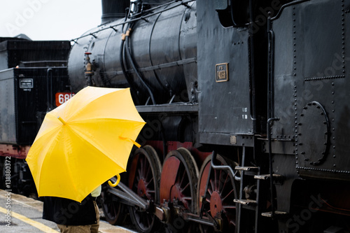 Man waiting with yellow umbrella on a train track.