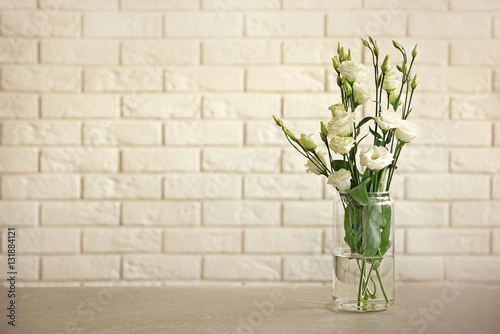 Glass vase with bouquet of beautiful flowers on brick wall background