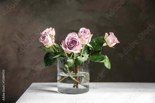 Glass vase with bouquet of beautiful roses on color background